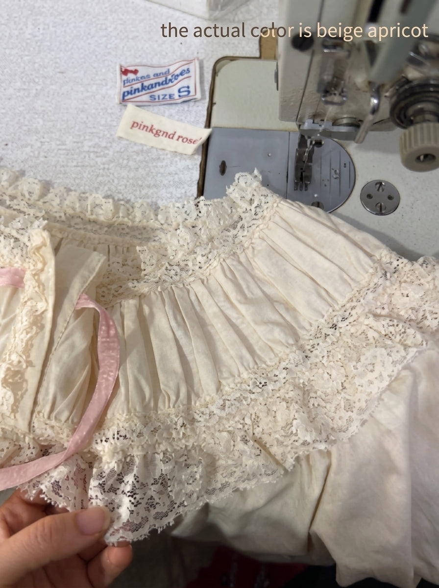Beige apricot lace ruffled panties held by a hand, with a sewing machine and sewing labels visible in the background. Text overlay reads 'the actual color is beige apricot'.