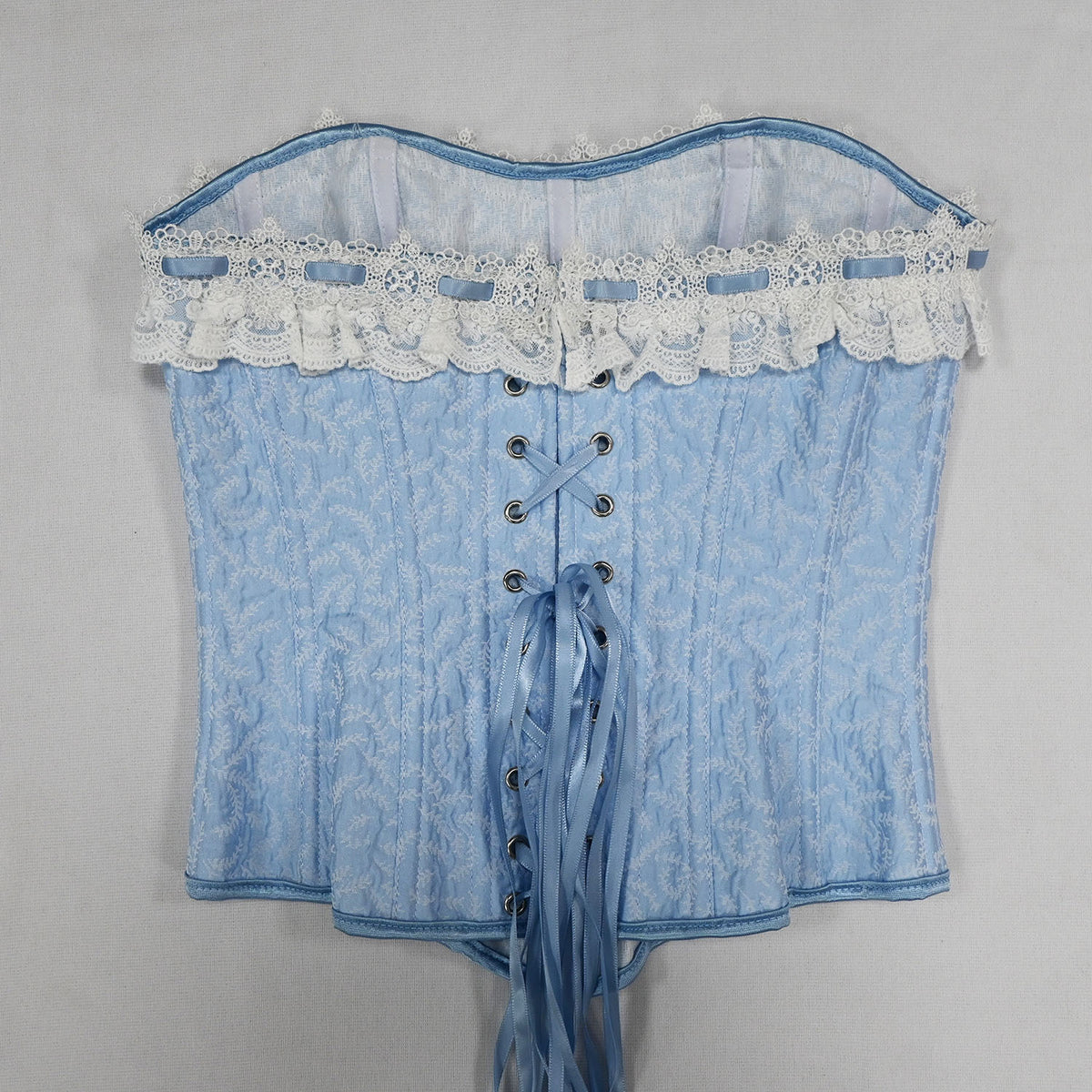 A light blue lace corset with a textured pattern, white floral lace trim, and a front lace-up closure with blue ribbons, shown against a plain light gray background.