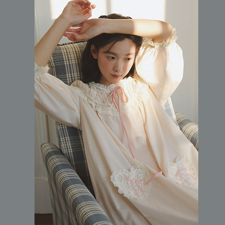 A young girl wearing a cream-colored nightgown with white lace trim and a pink ribbon tie, sitting in a plaid armchair.