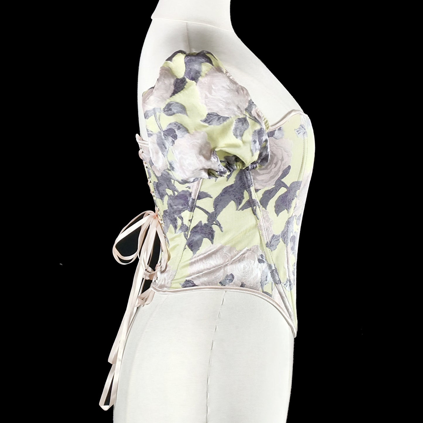 A strapless corset-style top with a pale yellow-green base and a gray floral print, displayed on a white mannequin against a black background.