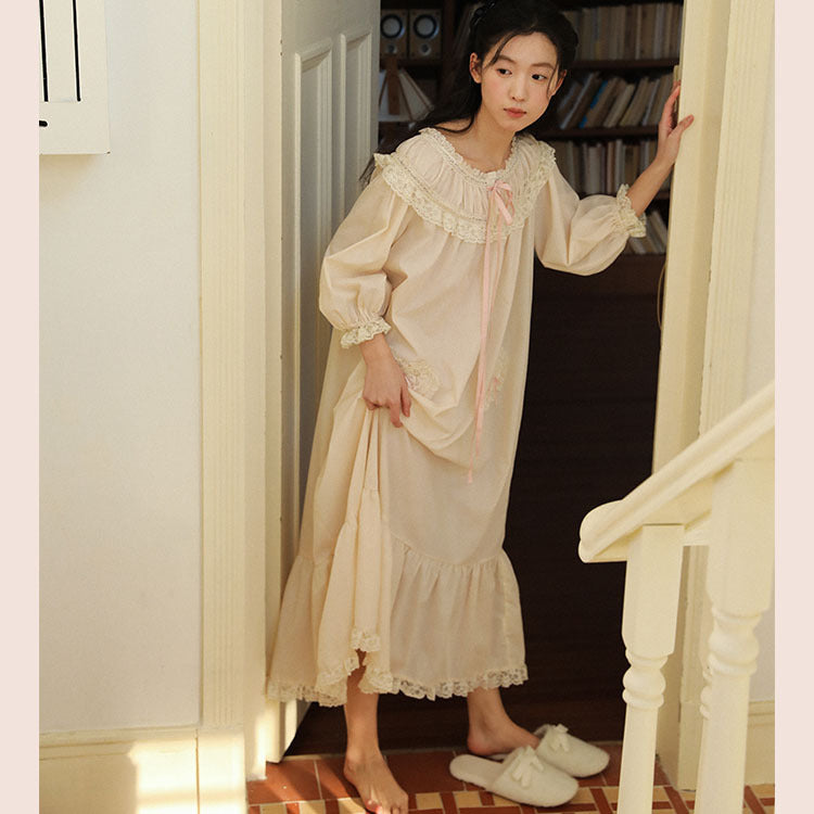 A woman wearing a long cream-colored nightgown with lace trim and a pink ribbon bow, standing in a doorway in a home setting.