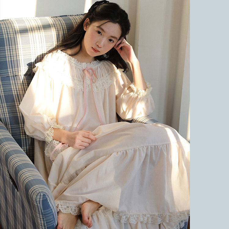 A young woman sits in a blue plaid armchair, wearing a long-sleeved cream-colored nightgown with lace trim and a pink ribbon detail.