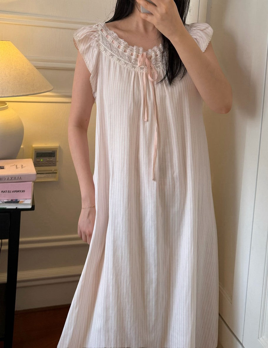 A woman wearing a light pink sleeveless nightgown with a ruffled lace-trimmed neckline and a tie at the chest, photographed indoors in a mirror selfie.