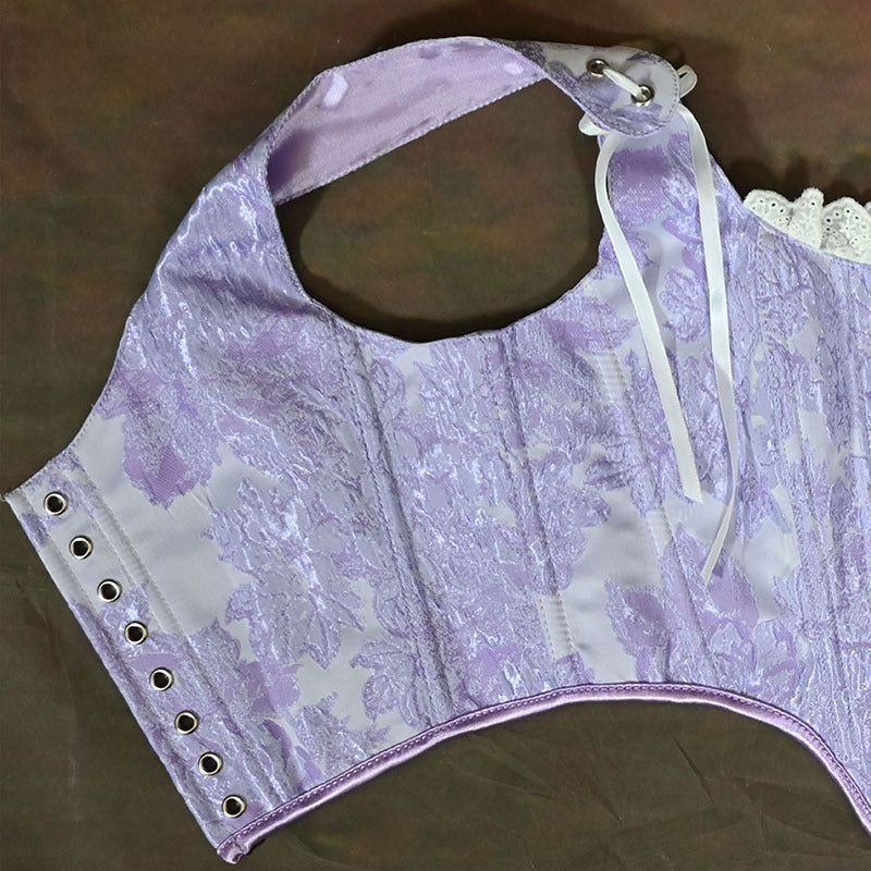 A lavender and white floral jacquard corset bustier top with lace-up front, eyelets on the side, and a white lace trim, laid flat on a brown surface.