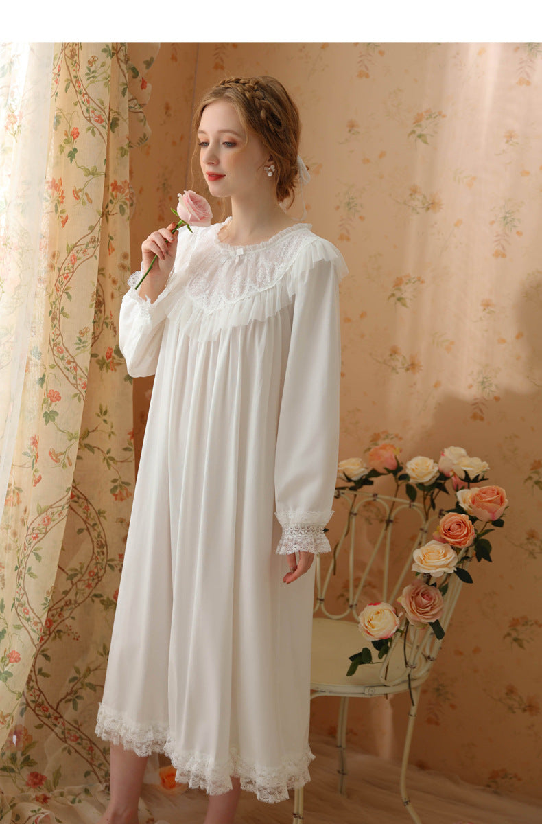 A woman wearing a long white nightgown with lace trim stands in a vintage-style room with floral wallpaper, holding a pink rose near her face.